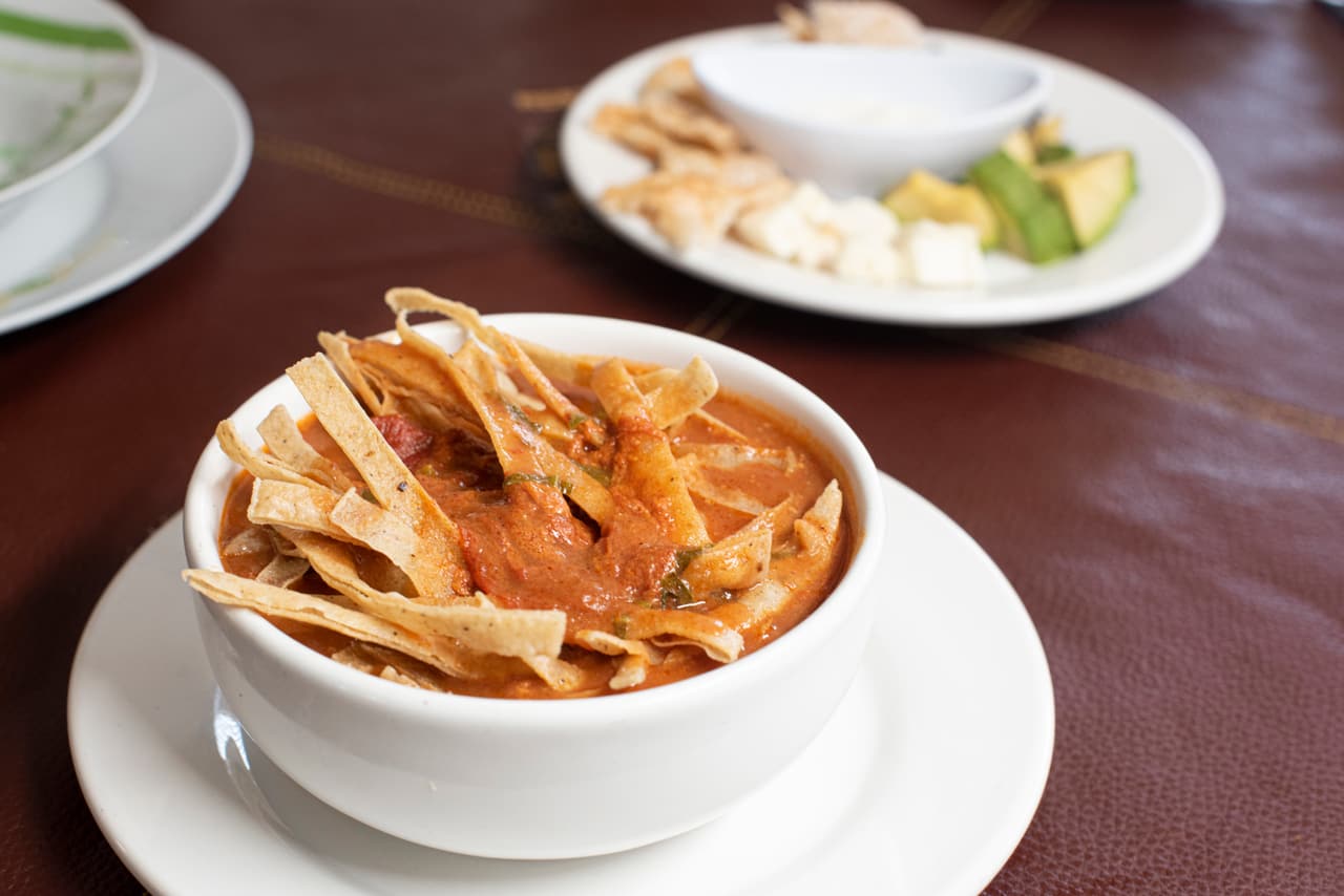 Sopa de tortilla con tiras de tortilla frita, aguacate, queso y crema